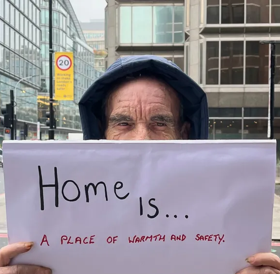 Homeless man holding a piece of paper that says 'Home is...'